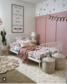 a bedroom with pink walls and white bedding, rugs and baskets on the floor