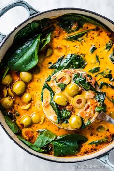 a pot filled with olives, spinach and cheese soup on top of a table