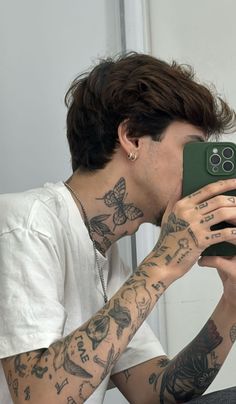 a man with tattoos taking a selfie in front of a mirror while holding his cell phone