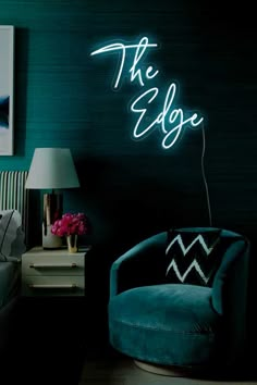 the edge neon sign is lit up in a dark room with a blue chair and lamp