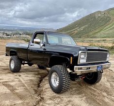 a black pickup truck parked on top of a dirt field next to a hill with hills in the background