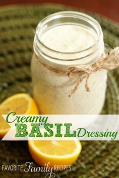 a mason jar filled with creamy basil dressing next to sliced lemons on a green place mat