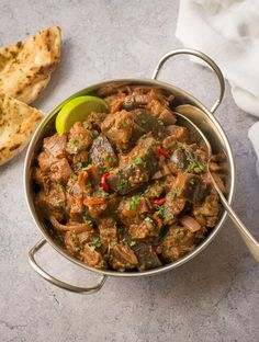 a pot filled with meat and vegetables on top of a table next to some bread