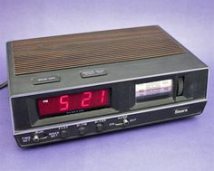 an alarm clock radio sitting on top of a purple tablecloth covered surface with the time displayed