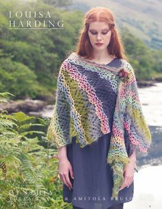 a woman wearing a crocheted shawl standing in front of a river and trees