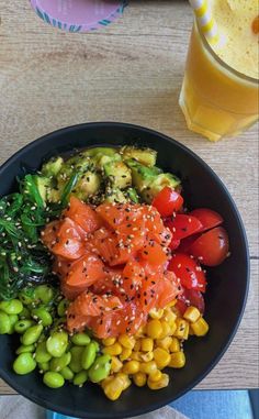 a black bowl filled with different types of food next to a glass of orange juice