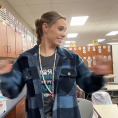 a woman standing in a classroom with her arms out and smiling at the camera while wearing a blue jacket