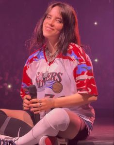 a woman sitting on the floor with her legs crossed and holding a microphone in front of her