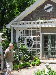 an older man standing in front of a house with a garden and gazebo on the side