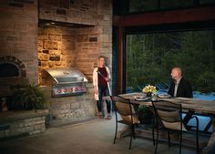 two people are sitting at a table in front of an outdoor grill