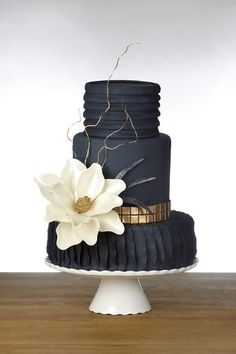 a three tiered cake with a white flower on top and black icing around the edges