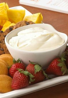 a white plate topped with cookies and fruit next to a bowl of whipped cream surrounded by sliced pineapples