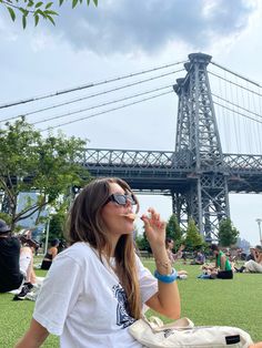 a woman sitting on the ground in front of a bridge and holding her hand up to her mouth