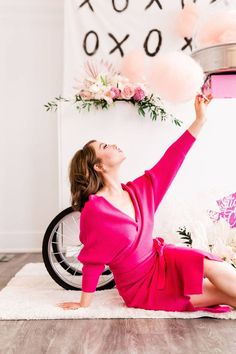 a woman in a pink dress is sitting on the floor with her legs crossed and arms up