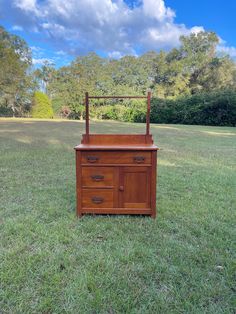 a wooden dresser sitting on top of a lush green field with trees in the background