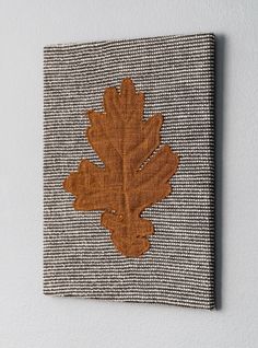 an embroidered oak leaf is mounted on the wall above a small piece of fabric that has been stitched together