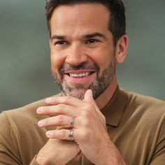 a man with a ring on his finger smiles at the camera while wearing a tan shirt