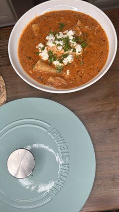 there is a bowl of soup next to a plate with bread on it and a spoon