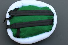 a green and white pillow with black straps on it's back end, sitting on a gray surface