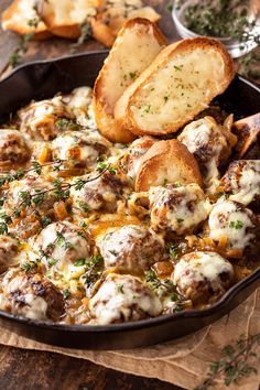 a pan filled with meatballs and bread on top of a wooden table next to garlic bread