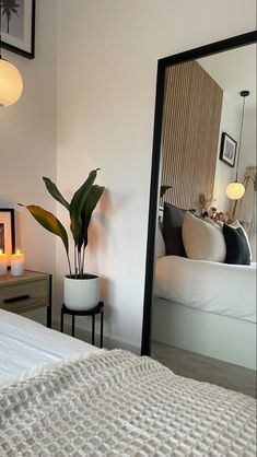 a bedroom with a bed, mirror and plants on the side table in front of it