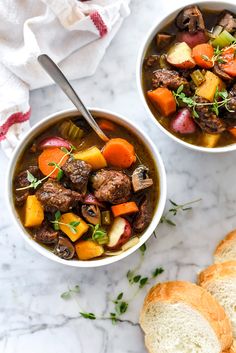 two bowls of soup with meat, potatoes and carrots on a marble counter top