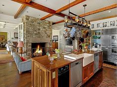 an open kitchen and living room area with wood floors, stone fireplace, and large windows