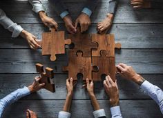 several people holding pieces of a puzzle together on a wooden table with their hands in the middle