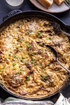 a casserole dish with meat and cheese in it on a table next to bread