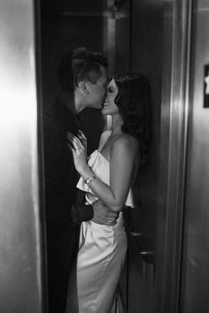 black and white photograph of a couple kissing in an elevator stall at the time of their wedding