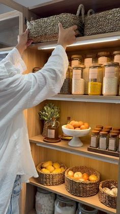 a woman standing in front of a shelf filled with lots of jars and baskets full of food