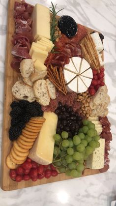 an assortment of cheeses, meats and grapes on a wooden platter with white marble counter top