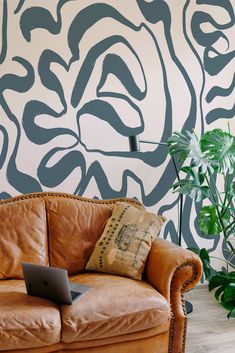 a couch with a laptop on it in front of a wall painted with black and white designs