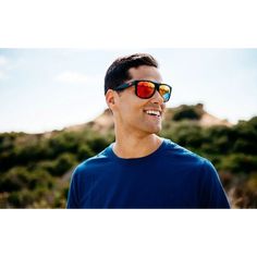 a man wearing red and blue sunglasses looking up at the sky with mountains in the background