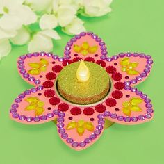 a small candle sitting on top of a pink flower shaped object with purple, yellow and red beads