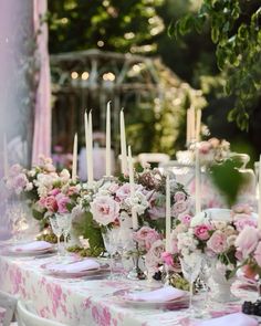 the table is set with pink and white flowers, candles, and glass vases