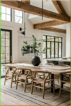 a dining room table with chairs and a vase on top of it in front of windows