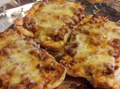 four pizzas sitting on top of a metal pan covered in cheese and meat toppings