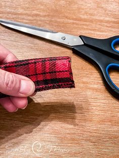 a pair of scissors being used to cut fabric with red and black checkered material