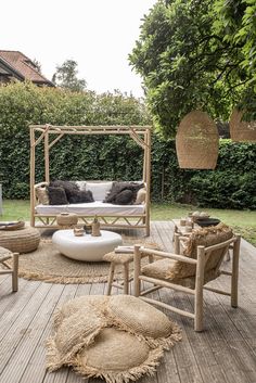 a wooden deck with chairs, tables and pillows on top of it in front of a green hedge