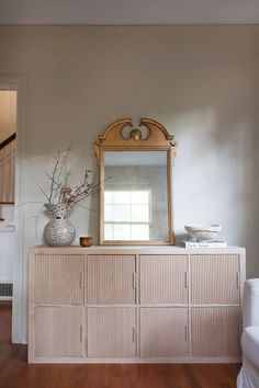 a dresser with a mirror and vase on top of it in a room that has hardwood floors