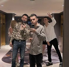 three men standing in front of a mirror taking a selfie with their cell phone