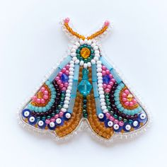 a beaded butterfly brooch sitting on top of a white surface