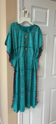 This Turquoise Blue cotton crew neck kaftan/bubu dress with hand crafted avocado pit button makes a realxed look. This soft cotton material makes it very gentle on the skin.  This printed cotton kaftan dress is good for vacation, loungewear, beach coverup, maternity dress, work from home. Size: Length 45 inches. Kaftans are usually very loose, and it is adjustable with a drawstring. Sides are finished with red pom pom style trim. This eco friendly avocado buttoned kaftan makes a Perfect gift for her! You can make a complete gift set for someone special with matching necklkace and earrings! Makes a nice gift!  will come in a nice wrapped gift package so it is ready to send as a gift to recipient directly For Matching Necklace and Earrings  see: https://www.etsy.com/listing/1790155231 https: Summer V-neck Kaftan For Home, Cotton V-neck Kaftan For Beachwear, Beach V-neck Kaftan Dress, Turquoise V-neck Kaftan For Summer, Summer V-neck Rayon Kaftan, Pom Pom Fashion, Cotton Kaftan Dress, Cotton Kaftan