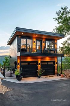 a two story house with black garage doors and windows on the second floor is lit up at night