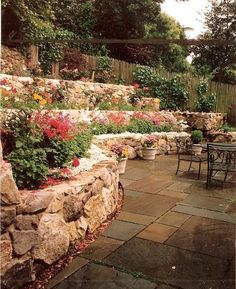 an outdoor patio with stone walls and flowers on the side walk, along with tables and chairs