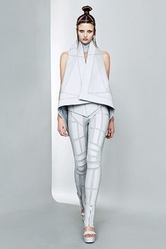 a model walks down the runway in white clothing with futuristic lines on her leggings