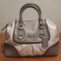 Ashley Spectator Leather Satchel Authentic, Tags Still On Style F17455 Silver Leather Looks Very Nice In Person, Pictures Don't Quite Capture The Metallic Sheen. Silvertone Hardware Height: 8" Width: 12" Depth: 4" Twin Handles 4" Drop Detachable Shoulder Strap Has Shoulder Pad At Center And Twin Swivel Dog Leash Trigger Clasps. Bottom Has Snaps Tabs That Will Store The Shoulder Strap When Unused. Interior Lined In Pink Satin Material. One Interior Zipper Pocket & One Open Pocket. Designer Silver Leather Bags, Designer Silver Bag With Detachable Strap, Luxury Leather Bag With Silver Accents, Elegant Leather Bags With Silver Accents, Coach Silver Leather Bag, Classic Coach Silver Bag, Silver Coach Leather Bags, Silver Leather Coach Bags, Silver Satchel Bag With Handles