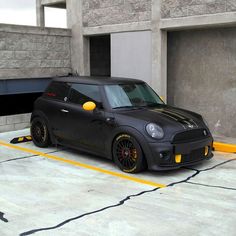 a black mini with yellow wheels parked in a parking lot next to a tunnel and building