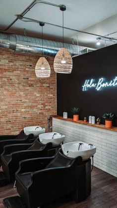 the interior of a barbershop with black chairs and white sinks in front of a brick wall